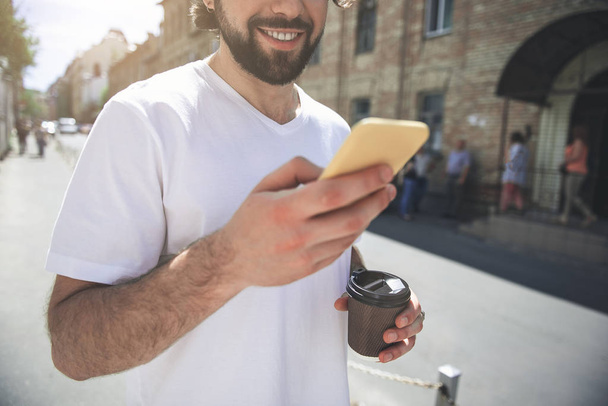 Smiling male person promenading with gadget and drink - Φωτογραφία, εικόνα