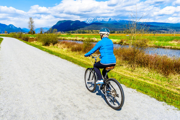 Ανώτερος γυναίκα ποδηλασία κατά μήκος του ποταμού Alouette για το ανάχωμα γύρω Πιτ πόλντερ στο την πόλη του Maple Ridge στην British Columbia, Καναδάς - Φωτογραφία, εικόνα