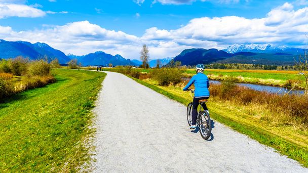 Senior vrouw fietsen langs de rivier van de Alouette op de dijk rond de Polder Pitt bij de stad van Maple Ridge in Brits-Columbia, Canada - Foto, afbeelding