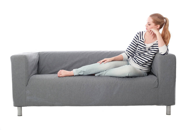 teljes hossza portré lány ül egy szürke kanapén, elszigetelt fehér stúdió háttere. - Fotó, kép