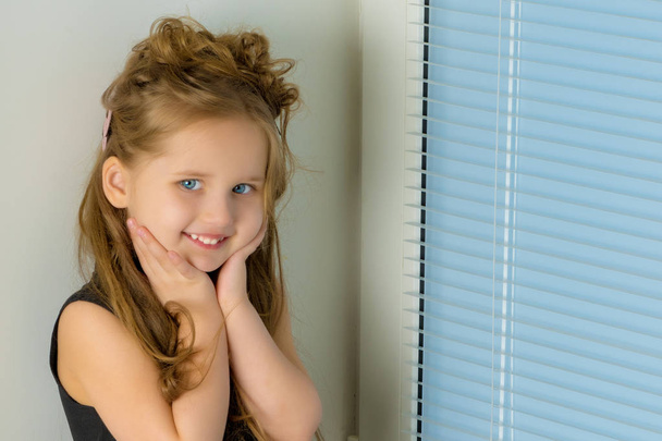A little girl is sitting on the window on the background of the  - Foto, imagen