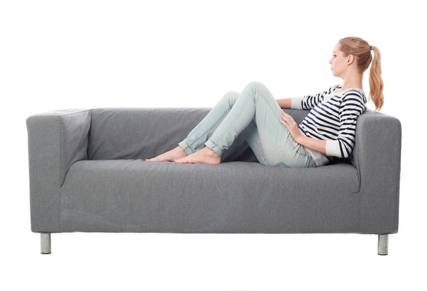 full length portrait of girl sitting on a grey couch, isolated on white studio background. - Foto, Bild