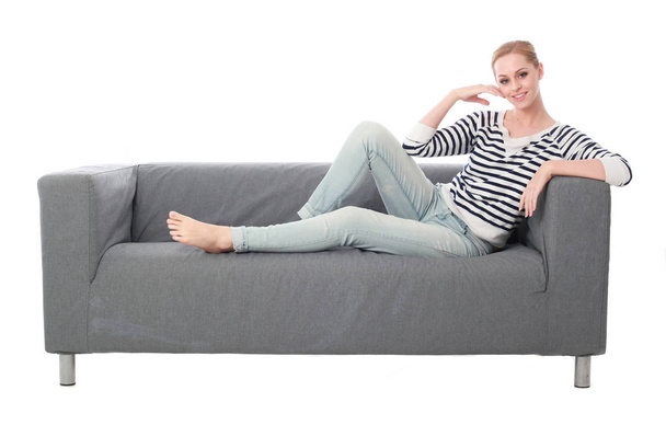 full length portrait of girl sitting on a grey couch, isolated on white studio background. - Photo, Image