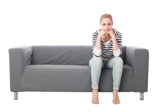Ganzkörperporträt eines Mädchens, das auf einer grauen Couch sitzt, isoliert auf weißem Studiohintergrund. - Foto, Bild