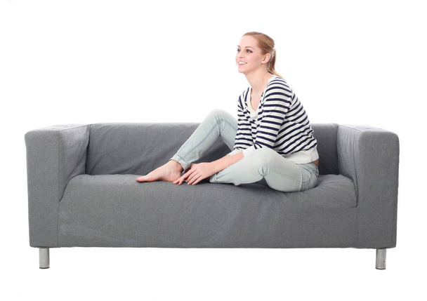 Ganzkörperporträt eines Mädchens, das auf einer grauen Couch sitzt, isoliert auf weißem Studiohintergrund. - Foto, Bild
