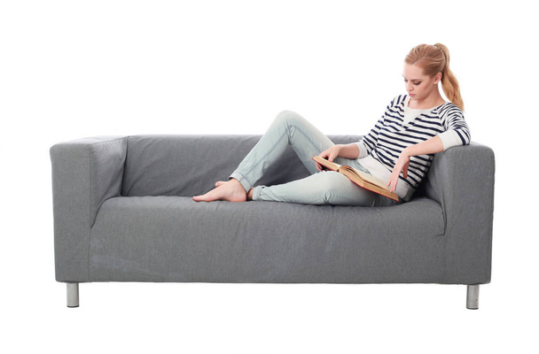 retrato de longitud completa de la niña sentada en un sofá gris, aislado en el fondo blanco del estudio
. - Foto, imagen
