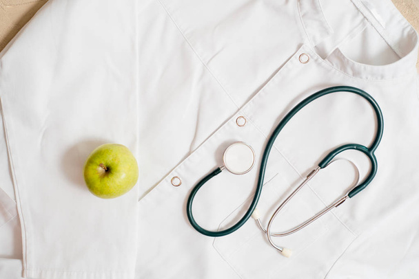 medical phonendoscope on a medical dressing gown. A green apple is a daisy flower. Concept of health. - Fotografie, Obrázek