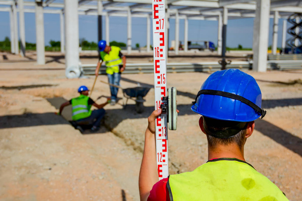 Bauarbeiter hält Richtstab, um Vermessungsingenieur, Geodäten zu helfen Position, Tiefe zu messen. - Foto, Bild