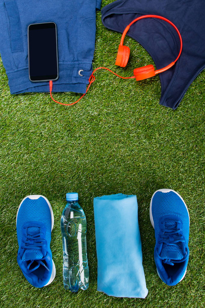 blue sportswear, a bottle of water and accessories for fitness, are arranged in a row against the background of grass - Fotó, kép