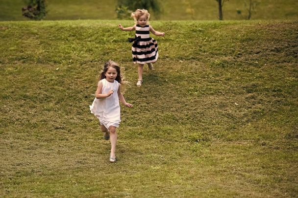Girls run from hill on green grass on summer day - Фото, изображение