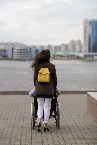 Taustakuva nuoresta naisesta kävelemässä vammaisen miehen kanssa pyörätuolissa laiturilla
 - Valokuva, kuva