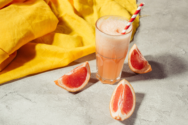 Glas met vers grapefruitsap op tafel met citrus stukken - Foto, afbeelding