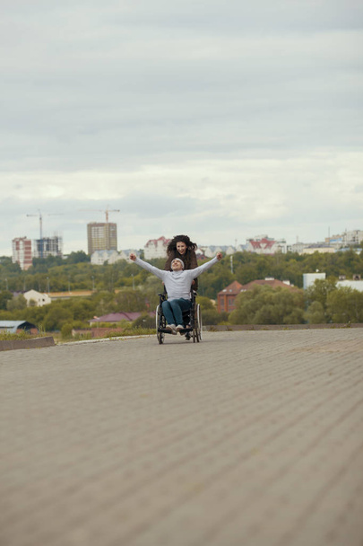 Fiatal nő, boldog fogyatékkal élő ember tolószékben szabadban szórakozik - Fotó, kép
