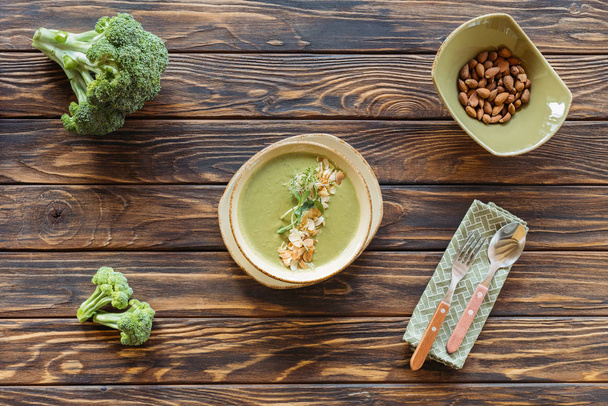 bovenaanzicht van vegetarische crème soep met broccoli, spruitjes en amandelen in kom op houten tafelblad - Foto, afbeelding