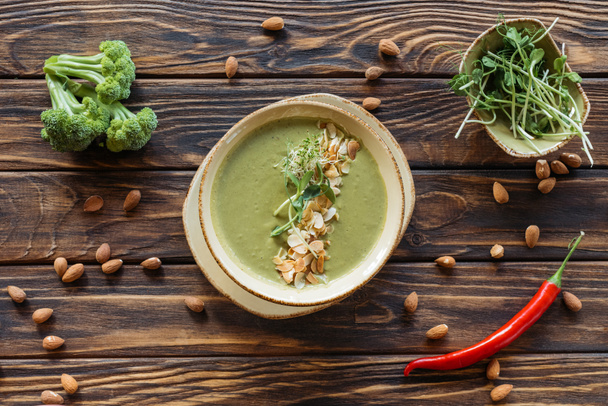 top view of arranged vegetarian cream soup, fresh broccoli, almonds and chili peppers on wooden surface - Foto, immagini