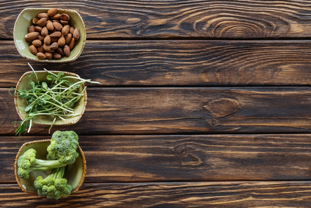 bovenaanzicht van amandelen, verse broccoli en spruiten in kommen op houten tafelblad - Foto, afbeelding