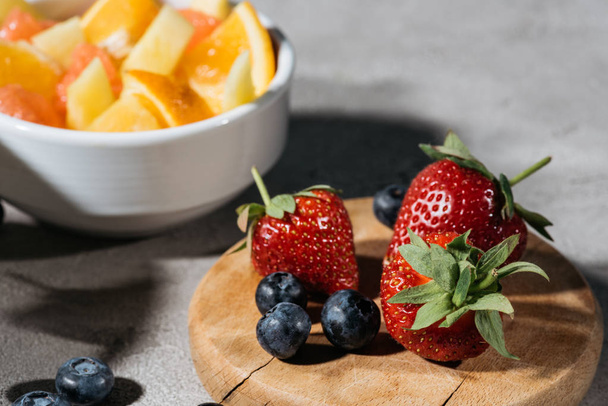 Strawberries and blueberries on wooden board by bowl with citrus fruits - Photo, Image