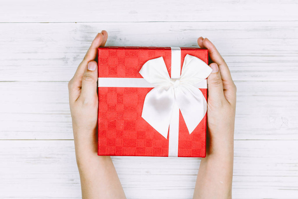 Χέρι που κρατά το κόκκινο δώρο κουτί με κορδέλα σε φόντο ξύλινη - Φωτογραφία, εικόνα