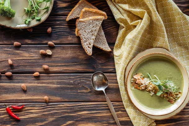 top view of arrangement of vegetarian cream soup with sprouts, pieces of bread and almonds on wooden surface - Foto, Imagen
