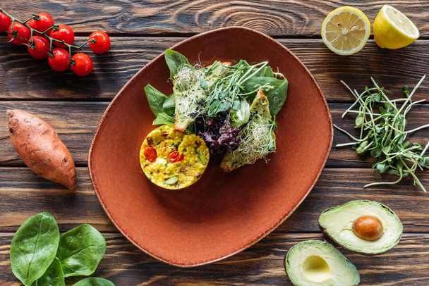 flat lay with vegetarian salad served on plate and fresh ingredients arranged around on wooden tabletop - Foto, Imagem