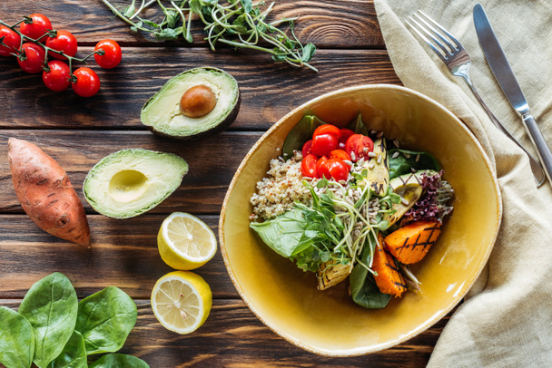 flache Lage mit vegetarischem Salat mit gegrilltem Gemüse und Rosenkohl, Bettwäsche und Besteck auf Holzoberfläche - Foto, Bild