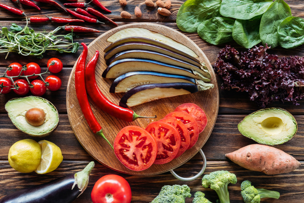 la puesta plana con berenjena cortada, tomates y chiles en la tabla de cortar con verduras frescas alrededor de la superficie de madera
 - Foto, Imagen