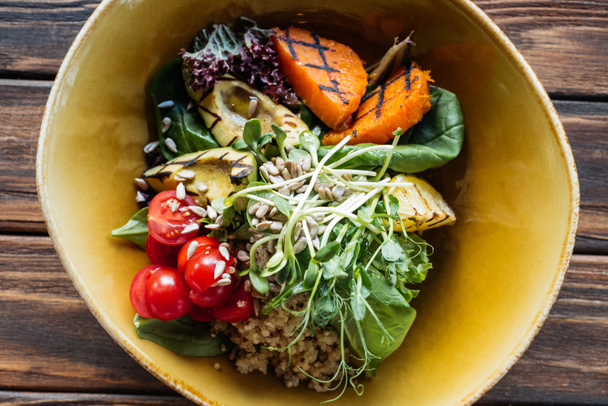 bovenaanzicht van vegetarische salade met gegrilde groenten, spruiten, cherry tomaten in kom op houten tafelblad - Foto, afbeelding