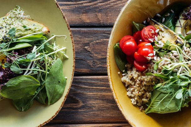vlakke leggen met vegetarische salades met spinazie en spruiten geserveerd in kommen op houten tafelblad - Foto, afbeelding
