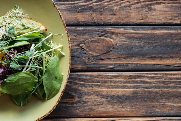 top view of vegetarian salad with spinach and sprouts on plate on wooden tabletop - Photo, Image