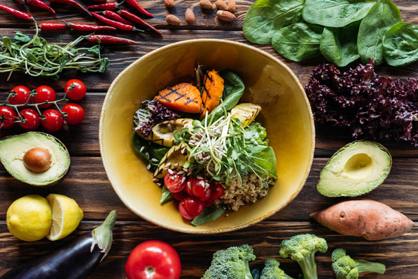 flat lay with vegetarian salad with grilled vegetables, sprouts, cherry tomatoes in bowl and arranged fresh ingredients around on wooden tabletop - Photo, Image