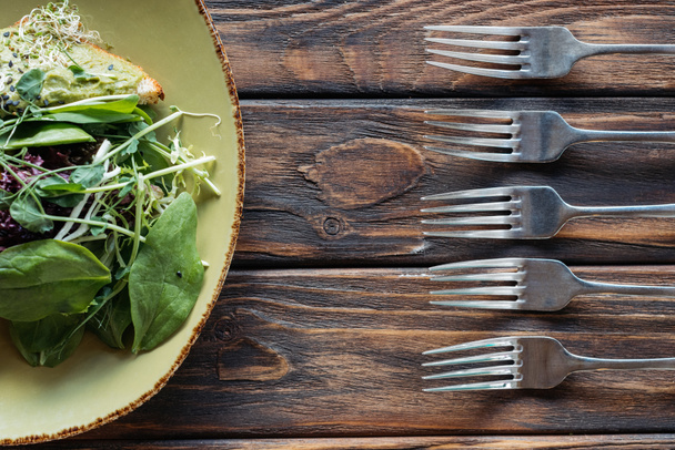 top view of vegetarian salad and arranged forks on wooden surface - Fotografie, Obrázek