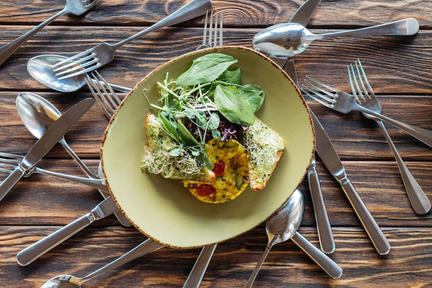 top view of vegetarian salad and arranged cutlery on wooden surface - 写真・画像