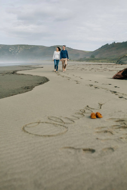 Parents marchant avec le nom de bébé Oliver écrit dans le sable
 - Photo, image