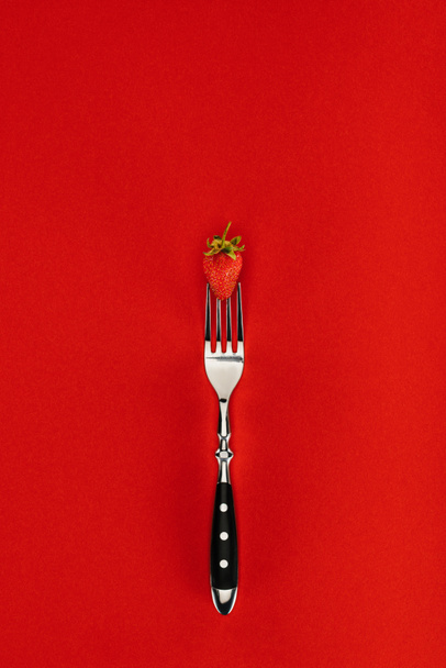 Fresa roja sobre un tenedor aislado sobre fondo rojo
 - Foto, imagen