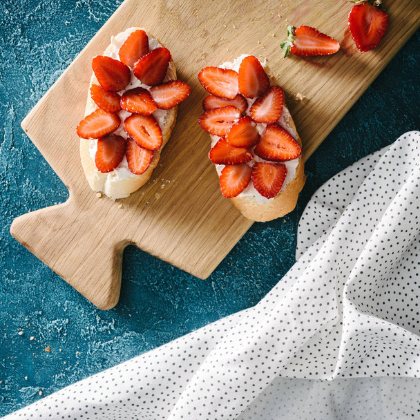 top view of baguette with cream cheese and raw strawberries on table with tablecloth - Фото, изображение