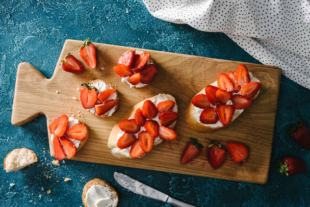 Breakfast of baguette with cream cheese and strawberries on cutting board - Foto, afbeelding