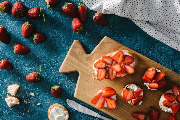 top view of bread with cream cheese and strawberries on wooden cutting board - Foto, Imagen
