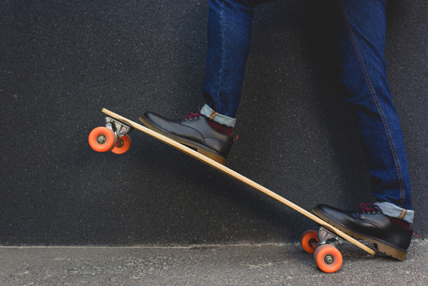 gedeeltelijke weergave van stijlvolle man permanent op skateboard op de straat    - Foto, afbeelding