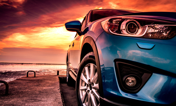 Blue compact SUV car with sport, modern, and luxury design parked on concrete road by the sea at sunset. Front view of beautiful hybrid car. Driving with confidence. Travel on vacation at the beach. - Photo, Image