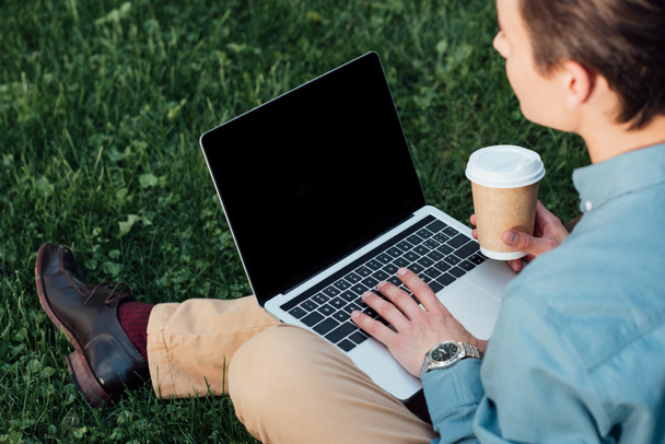 tiro recortado de freelancer beber café e usando laptop na grama
 - Foto, Imagem