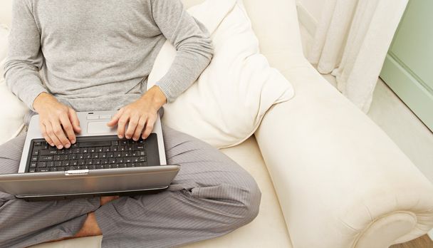 cuerpo del hombre sentado en un sofá blanco y el uso de una computadora portátil
. - Foto, imagen
