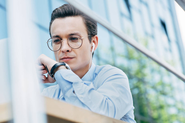 selective focus of young businessman in eyeglasses using laptop outside modern building - Фото, изображение