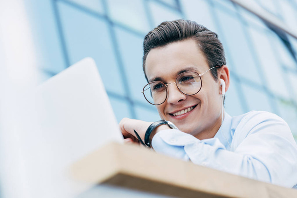 bel homme d'affaires souriant dans les lunettes à l'aide d'un ordinateur portable à l'extérieur, mise au point sélective
 - Photo, image