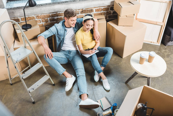 high angle view of young couple sitting on floor while moving into new home - Photo, Image