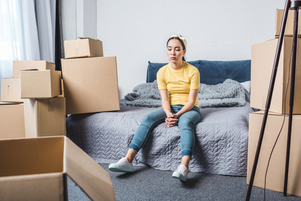 exhausted young woman surrounded with boxes relaxing on bed after relocation - Photo, Image