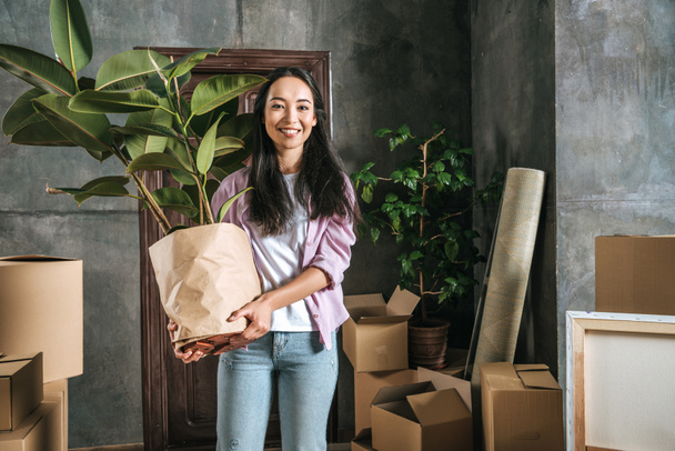happy young woman with ficus plant and boxes moving into new house - Fotoğraf, Görsel