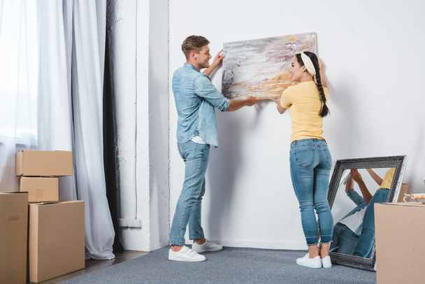 beautiful young couple hanging picture on wall together while moving into new home - Foto, afbeelding