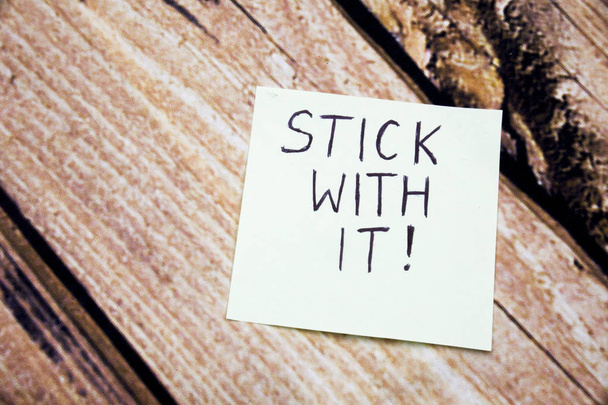 Handwritten motivational message on the white paper. Stick with it message on the paper with retro wooden bark background. Conceptual messages written on the white paper. - Photo, Image