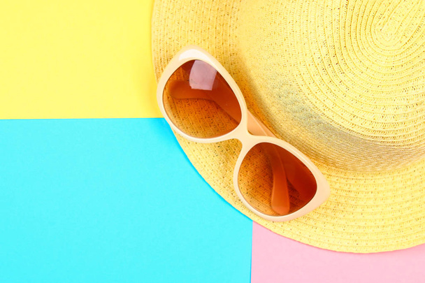 Hat, sunglasses on a three-color pastel background of blue, yellow and pink - Фото, зображення