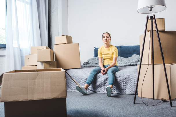 tired young woman surrounded with boxes relaxing on bed after relocation - Foto, Bild